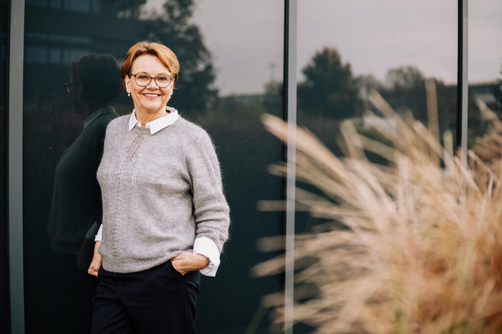 Frau lächelt vor Glasfassade.